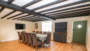 A dining room with a wooden table and chairs, a television on the wall, and a green door. - Trewen (Pwllheli)