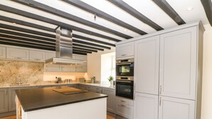 A modern kitchen with a central island, built-in oven, and stainless steel appliances. - Trewen (Pwllheli)