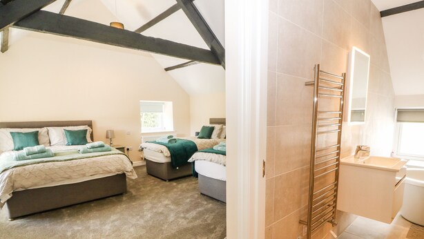 A bedroom with two beds, a bathroom with a towel rack, and a window. - Trewen (Pwllheli)