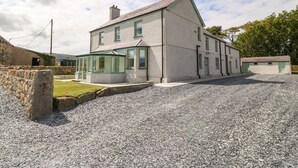 A two-story house with a covered patio and a gravel driveway. - Trewen (Pwllheli)