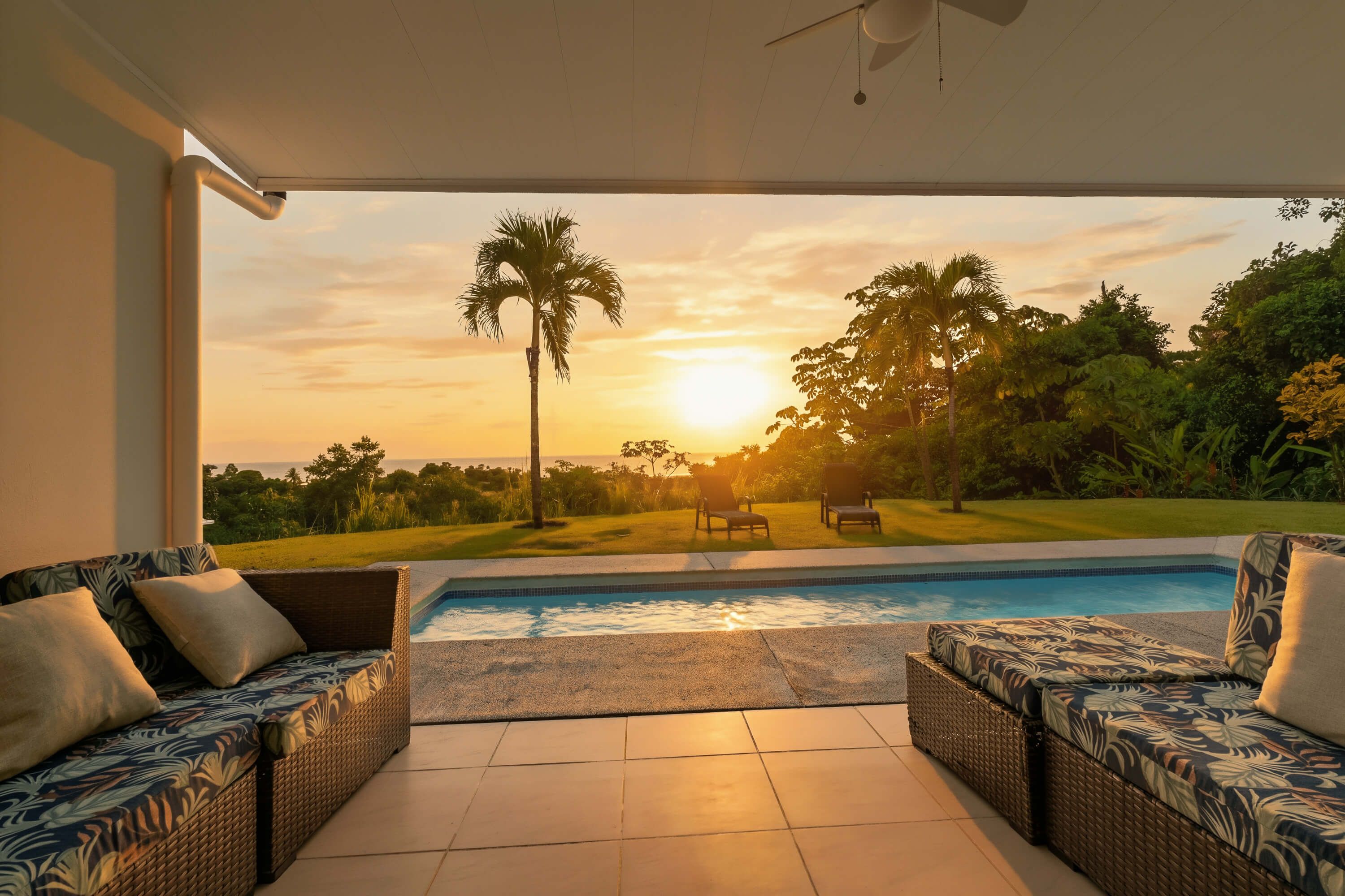 A pool area with two wicker sofas and a view of a golf course at sunset.