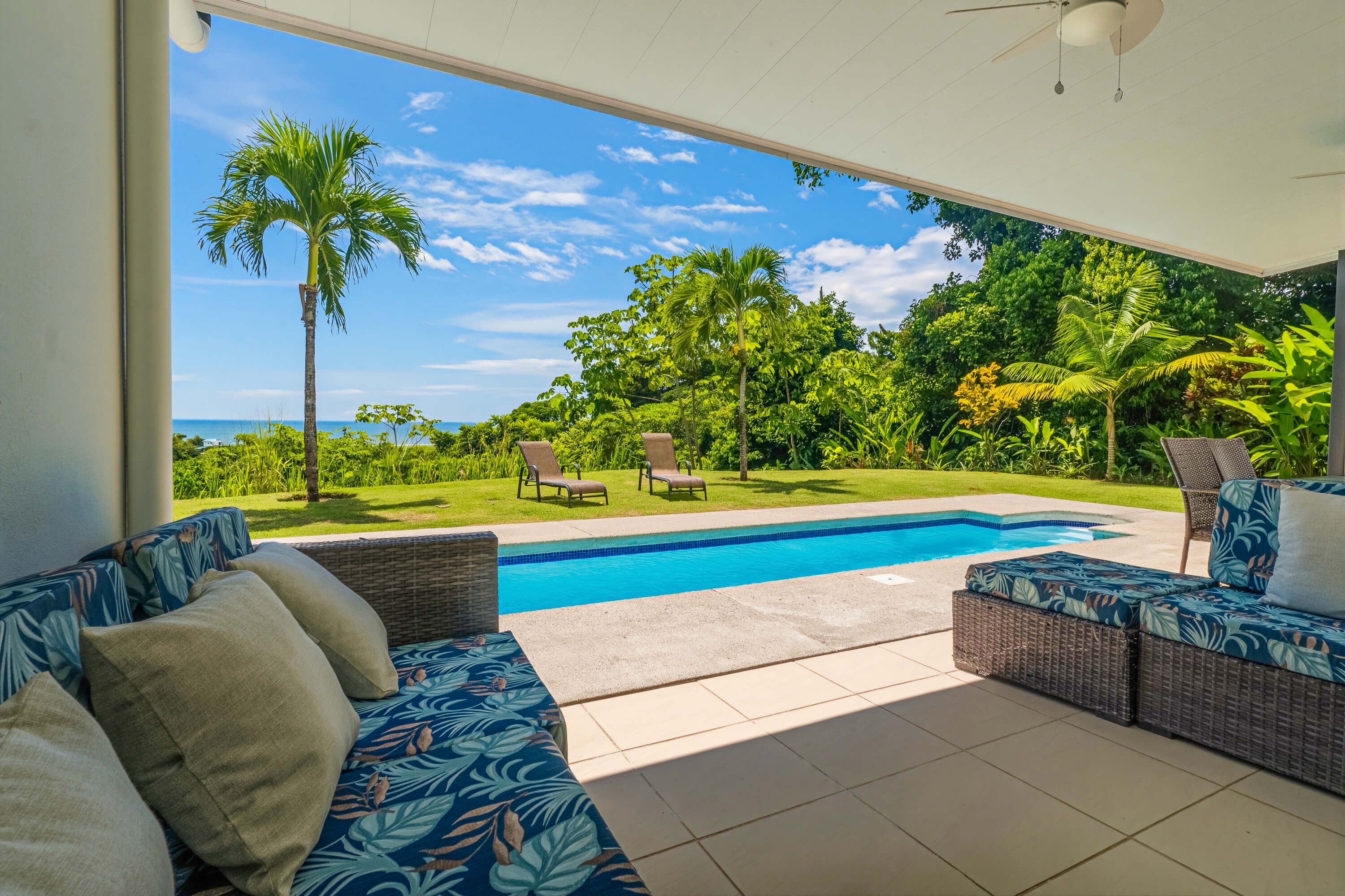 A poolside area with a view of the ocean, a pool, and outdoor furniture.