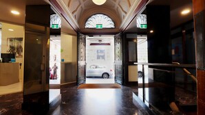 Un hall d’hôtel avec un sol en marbre, un comptoir d’accueil et un escalier menant aux étages supérieurs.