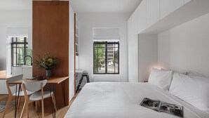 Une chambre moderne avec un grand lit, un bureau et une chaise. Une fenêtre offre une vue sur les bâtiments environnants.