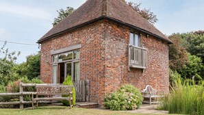A brick building with a small balcony, a wooden bench, and a garden area. - Dovecote (Dover)