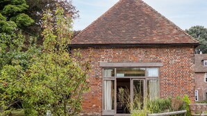 A brick building with a tiled roof, a wooden fence, and a pathway leading to the entrance. - Dovecote (Dover)