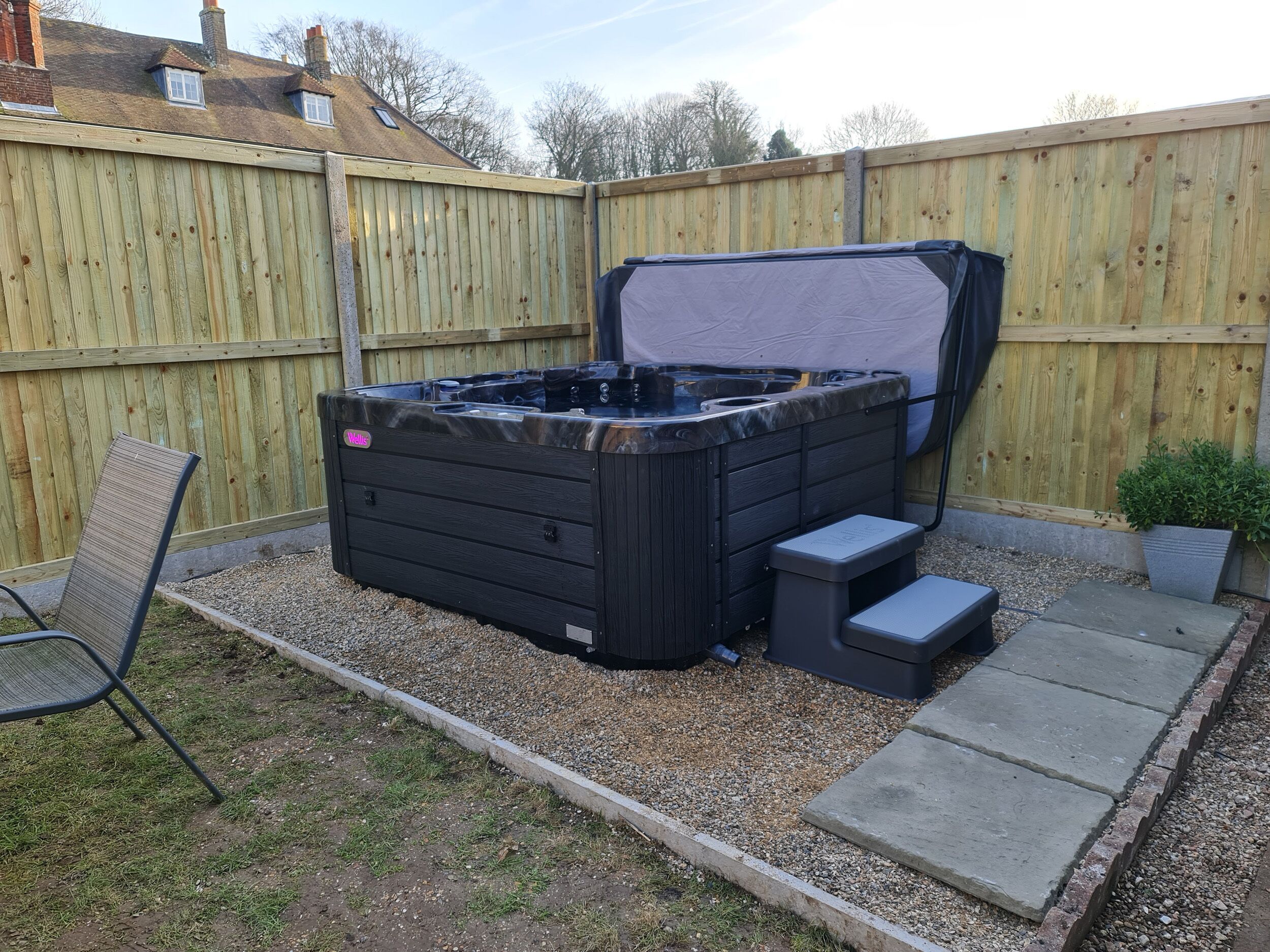 A hot tub in a backyard with a wooden fence, a chair, and a small step leading to the hot tub.