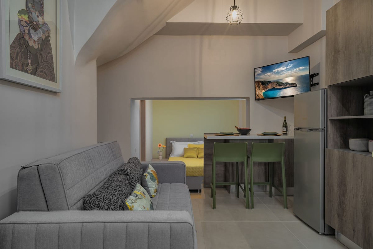 Un espace de vie compact comprenant un canapé, un coin repas avec une table et des chaises, un lit, une cuisine avec un réfrigérateur et un téléviseur fixé au mur.