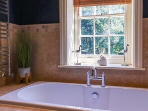 A bathroom with a large bathtub, a window with a view of greenery, and a potted plant.