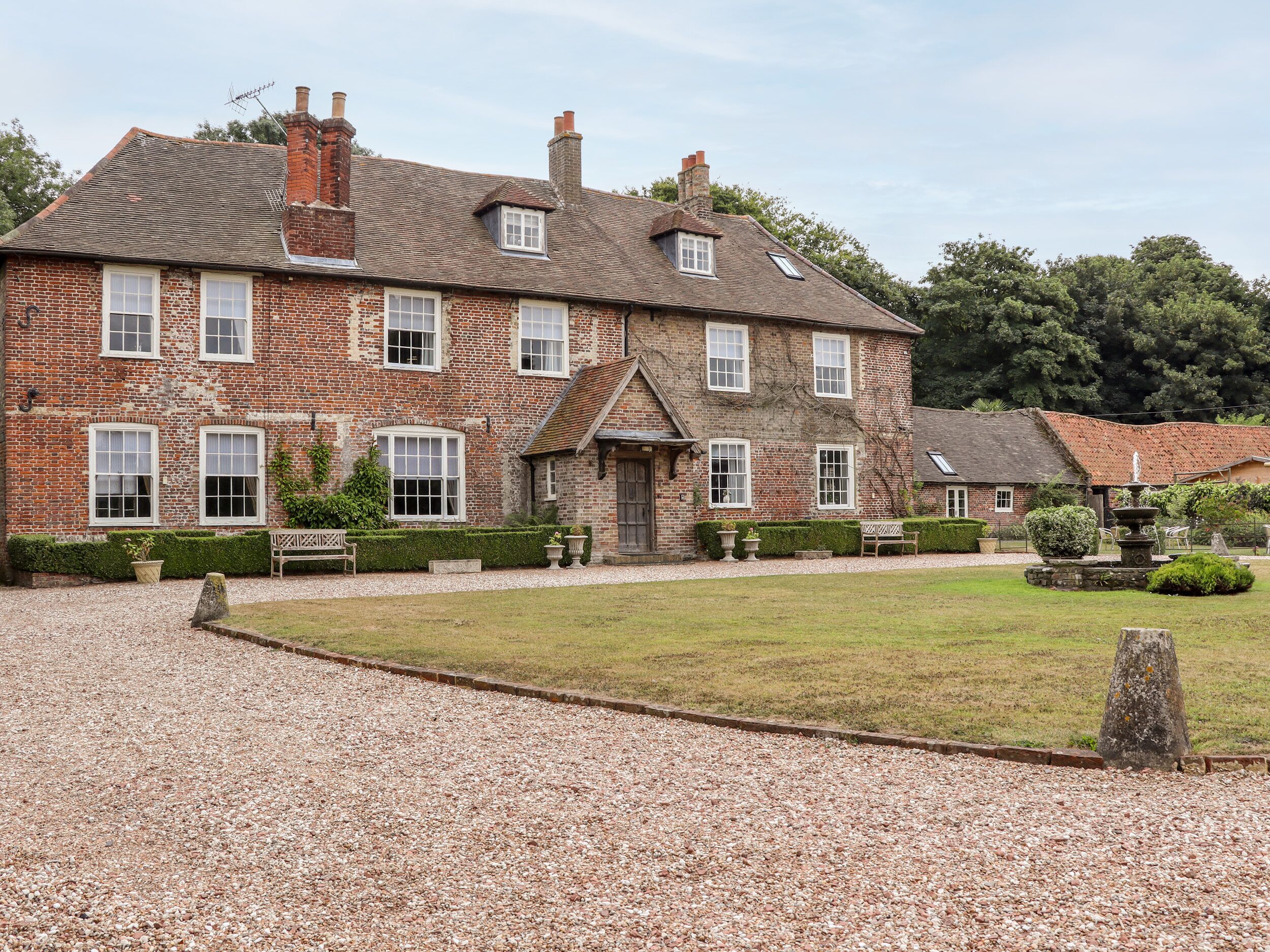 A large brick house with multiple windows, a gravel driveway, and a well-maintained lawn.