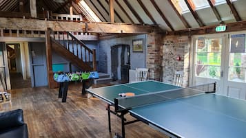 Una habitación con mesa de ping pong, mesa de futbolín y una escalera que sube a un nivel superior.
