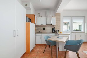 Une cuisine moderne avec des armoires blanches, un mur d’accent en bois, une table à manger avec deux chaises et une vue sur l’extérieur par une fenêtre.