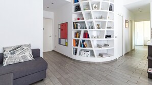 En moderne stue med en grå sofa, en hvid buet reol fyldt med bøger og dekorative genstande, samt et flisegulv.