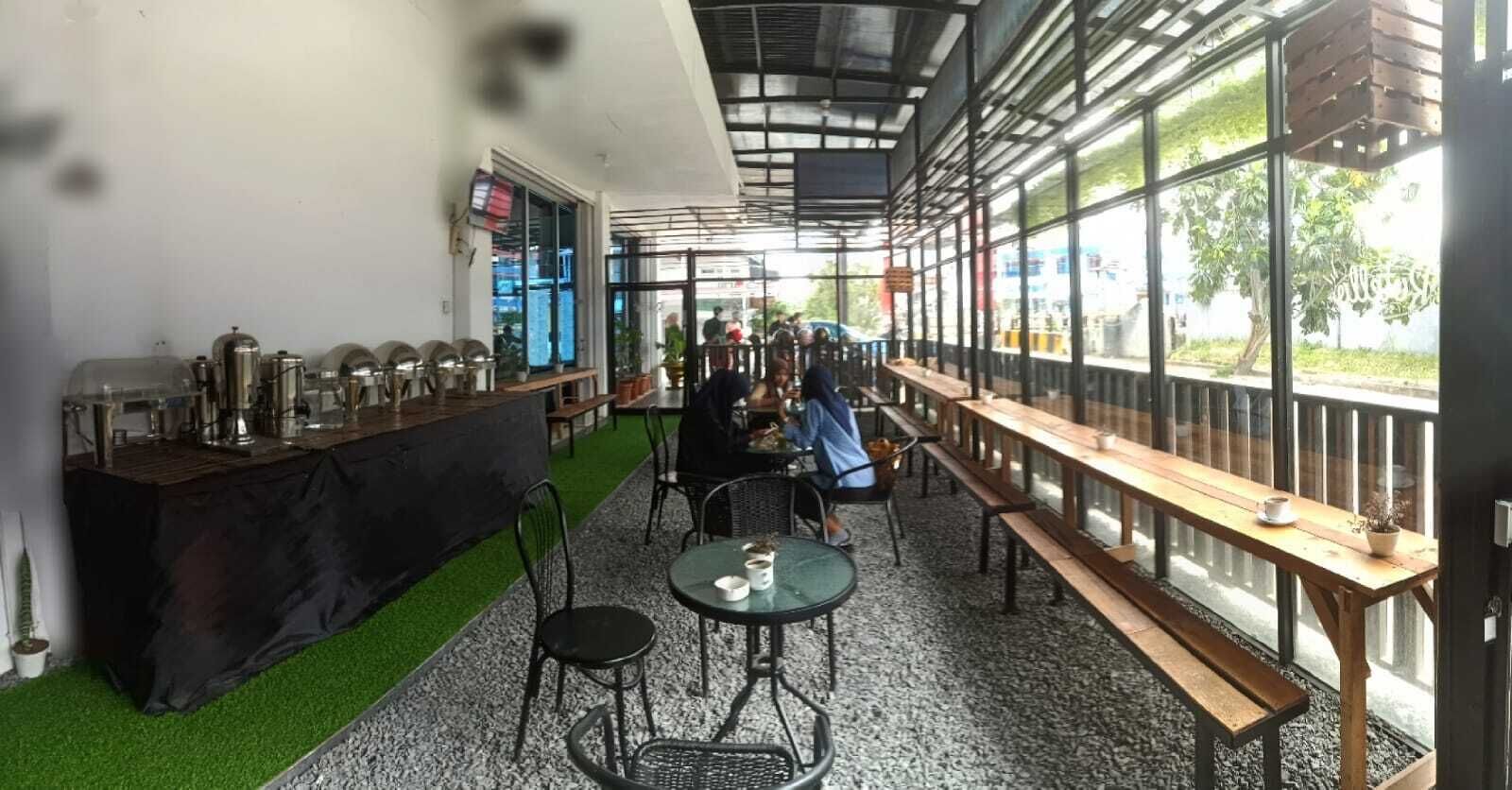 An indoor cafe with tables and chairs, a counter with kitchen equipment, and large windows.