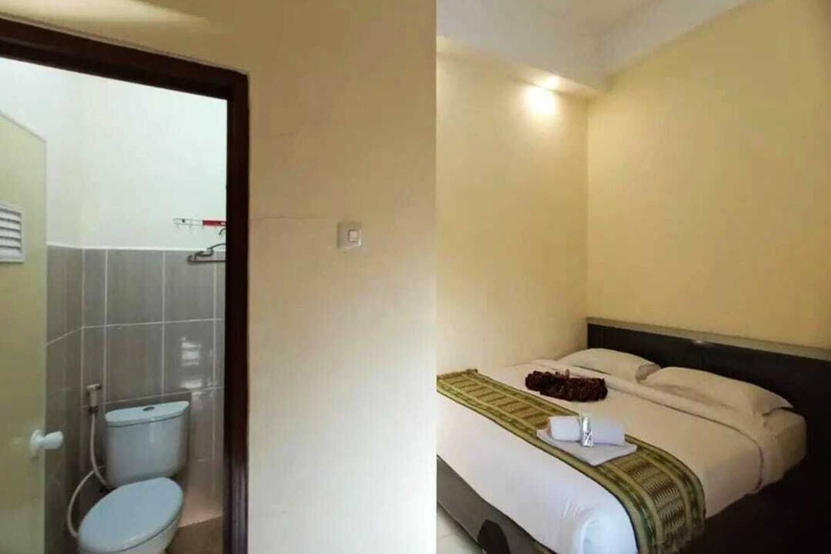 A hotel room with a toilet, a bed with a green blanket, and a headboard.