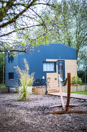 A modern blue and wooden house with a patio, a hammock, and a small garden. - La tiny house exiguë (Saint-Blimont)