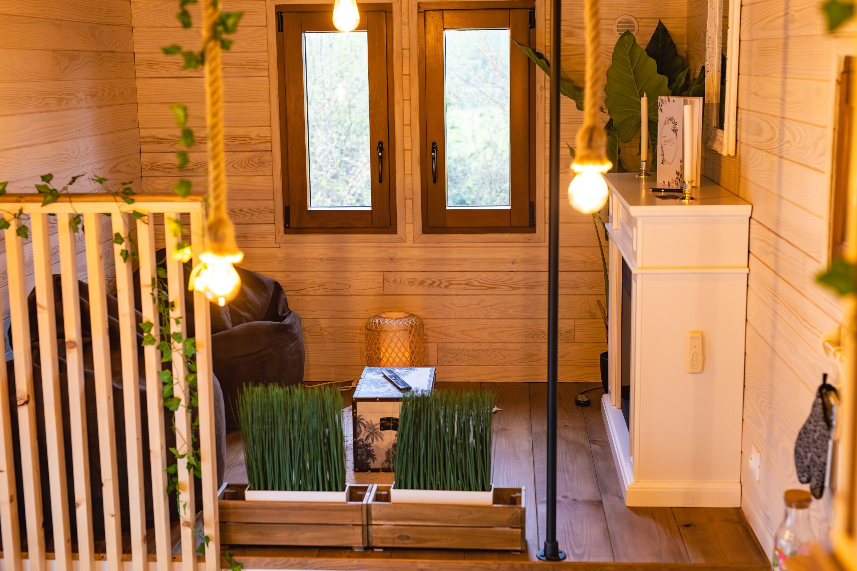 Un intérieur en bois avec deux fenêtres, un canapé, une petite table et un meuble.