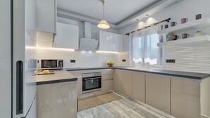 A modern kitchen with white cabinetry, a microwave, an oven, and a countertop with a fruit bowl. - Villa Agalliu (Zakynthos)