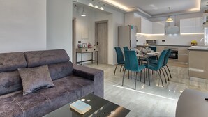 A modern living room with a grey sofa, a coffee table with a book, and teal chairs around a dining table. - Villa Agalliu (Zakynthos)