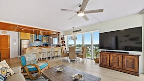 Ein geräumiges Wohnzimmer mit großem Fernseher, Deckenventilator aus Holz und Blick auf die Stadt.