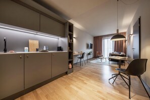 Eine moderne Küche mit eingebauten Geräten, ein Essbereich mit Tisch und Stühlen sowie ein Wohnzimmer mit Sofa und Fernseher.