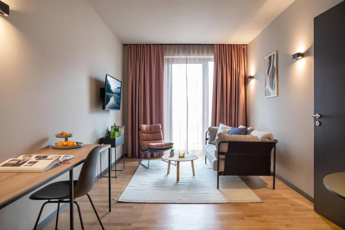 Ein modernes Wohnzimmer mit einer Couch, einem Couchtisch, einem an der Wand montierten Fernseher und einem Essbereich mit Tisch und Stühlen.
