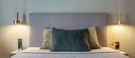 Una cama bien hecha con cabecera gris, dos lámparas de noche y un libro sobre la cama.