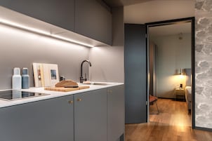 A modern kitchen with a built-in stove, a sink, and a cutting board with bread. There are books and bottles on the counter.