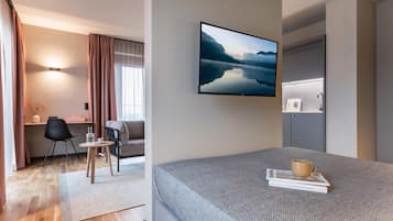 A modern hotel room with a bed, a desk, a chair, a sofa, and a large window with curtains.