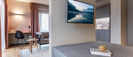 Habitación de hotel moderna con cama, escritorio, silla, sofá y un gran ventanal con cortinas.