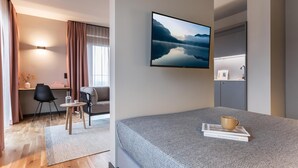 A modern hotel room with a bed, a desk, a chair, a coffee cup, and a framed picture on the wall.