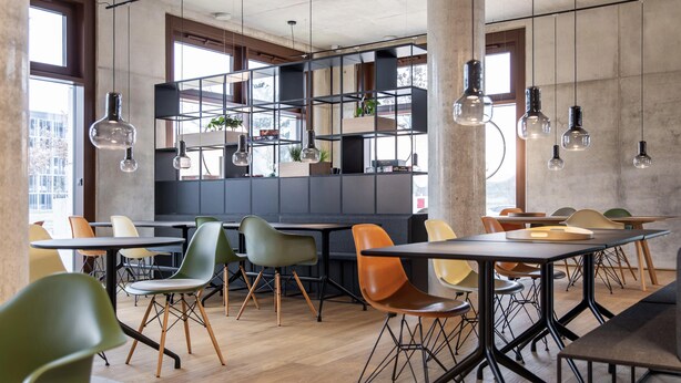 A modern dining area with tables, chairs, hanging lights, and a view through large windows.