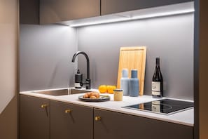 Eine moderne Küche mit Spüle, einem schwarzen Wasserhahn, einem Holzer Schneidebrett, einer Weinflasche und einem Teller mit einem Croissant.