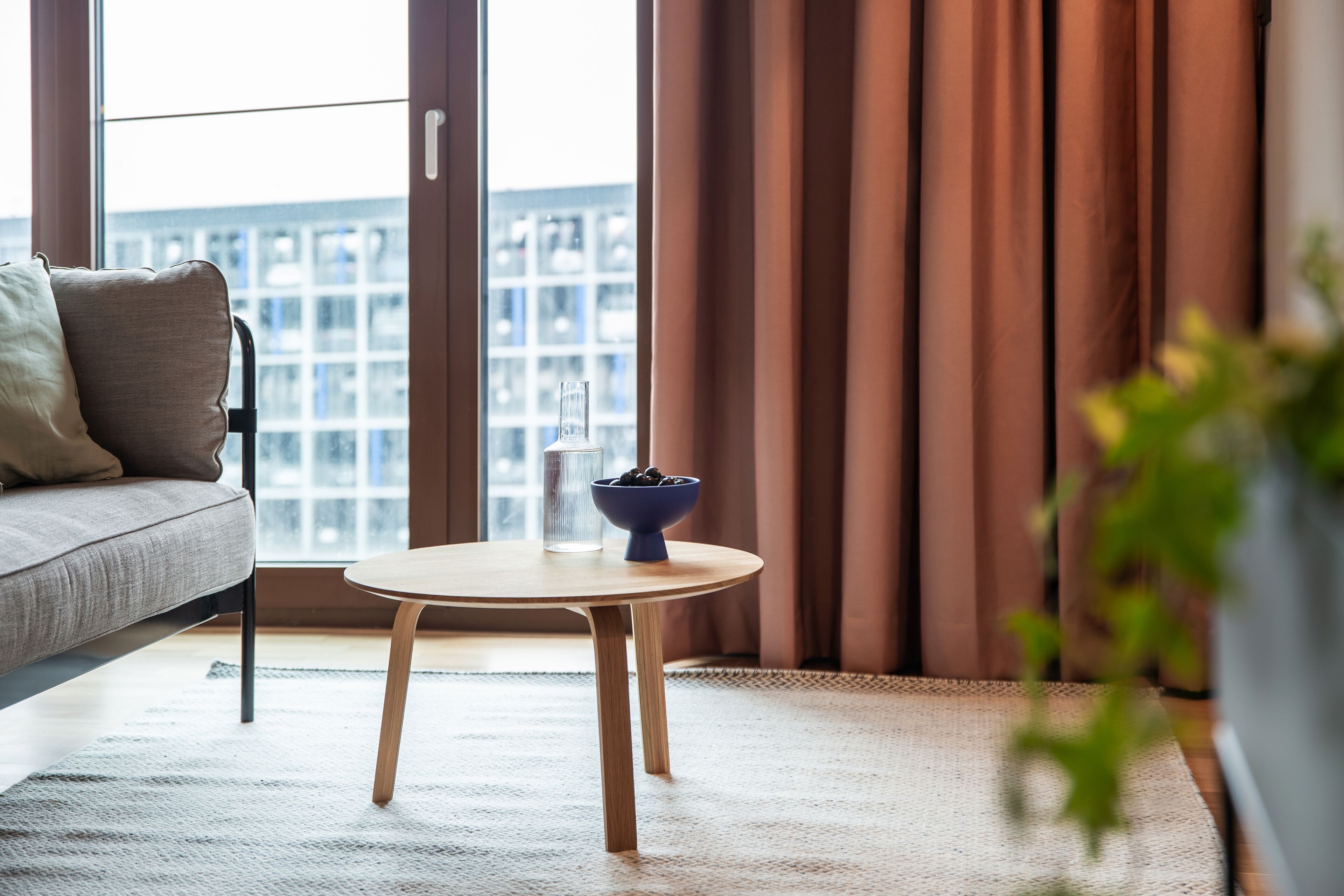 A modern living room with a sofa, a round wooden table, and a bowl of fruit.