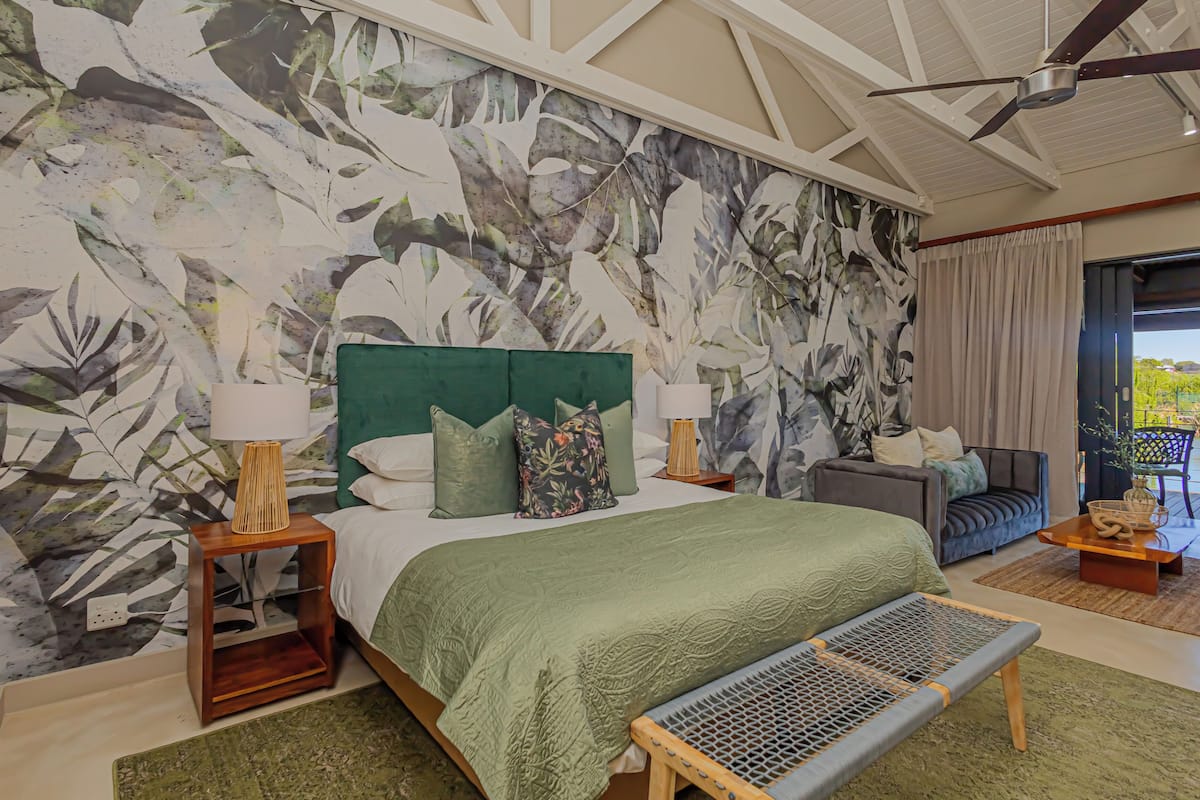 Een slaapkamer met een groot bed, twee nachtkastjes, een bankje, een sofa en uitzicht op het omliggende landschap.
