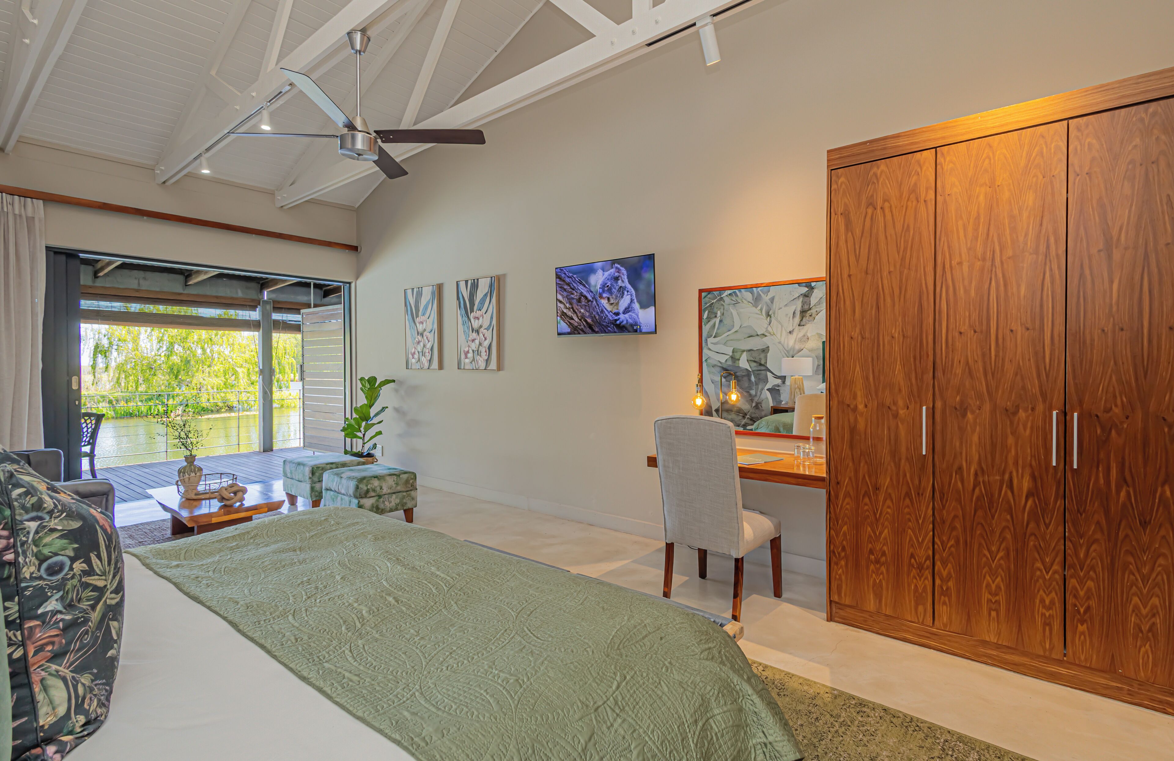 A bedroom with a bed, a desk, and a wardrobe. There is a window with a view of greenery outside.