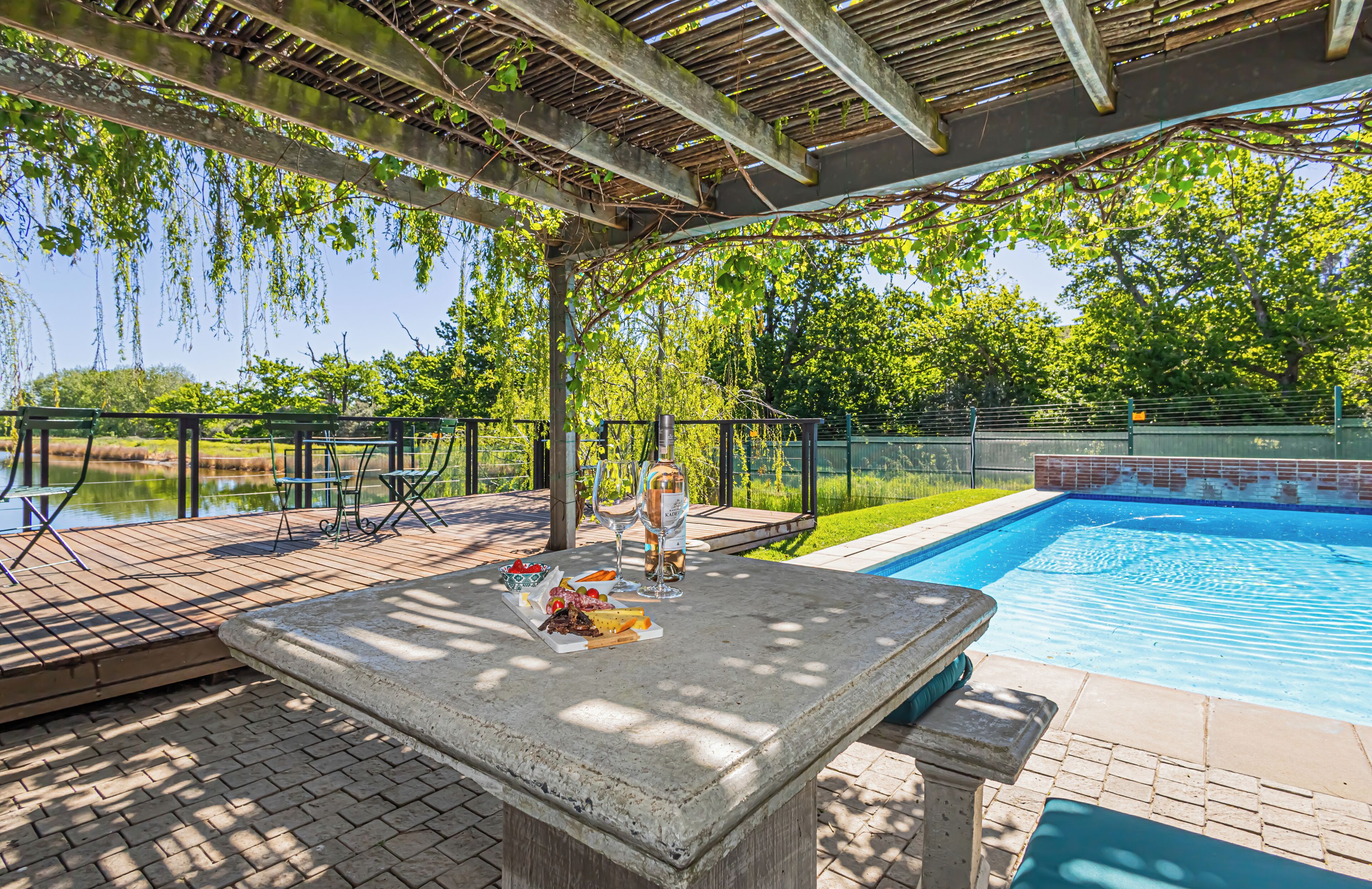 Zona de piscina exterior con una pérgola, asientos y una mesa con comida y bebidas.