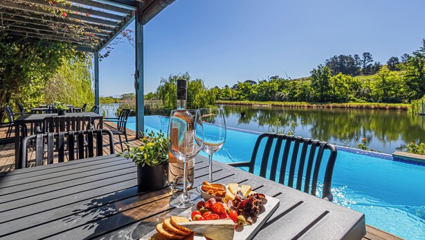 An outdoor dining area with a pool view, wooden tables, and chairs.