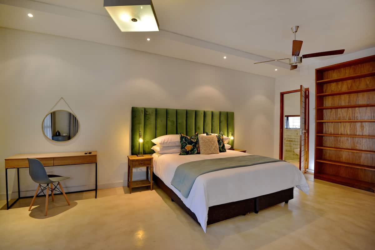 Een slaapkamer met een bed, bureau, stoel en een spiegel.