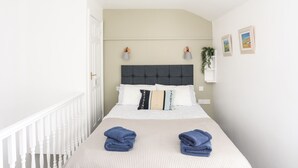 A bedroom with a bed, two wall-mounted lamps, a hanging plant, and a white railing. - 2 The Coach House (Pentraeth)