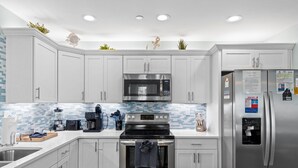 A modern kitchen with white cabinets, stainless steel appliances, a tiled backsplash, and a stainless steel refrigerator with magnets and papers.
