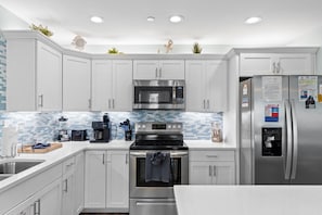 A modern kitchen with white cabinets, stainless steel appliances, a tiled backsplash, and a stainless steel refrigerator with magnets and papers. - Just Beachy Private Pool! Just 20 Steps to the beach! Incredible Home (PANAMA CITY BEACH)