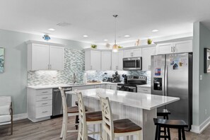 A modern kitchen with white cabinetry, a central island, stainless steel appliances, and a tiled backsplash. - Just Beachy Private Pool! Just 20 Steps to the beach! Incredible Home (PANAMA CITY BEACH)