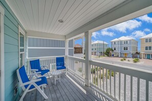 A covered porch with blue chairs and a table, overlooking a residential area with houses.