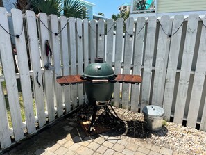 A barbecue grill with a wooden tray and a metal pot, set against a white picket fence.