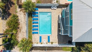An aerial view of a swimming pool area with lounge chairs, a small deck, and a building with a sloped roof.