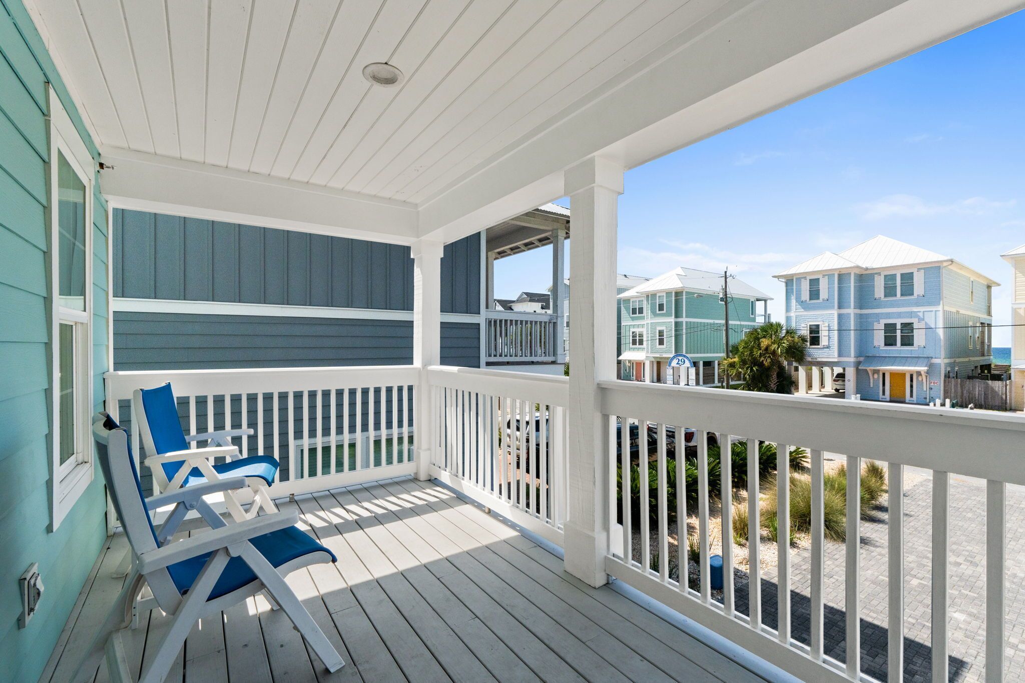 A covered porch with white railings and blue chairs.