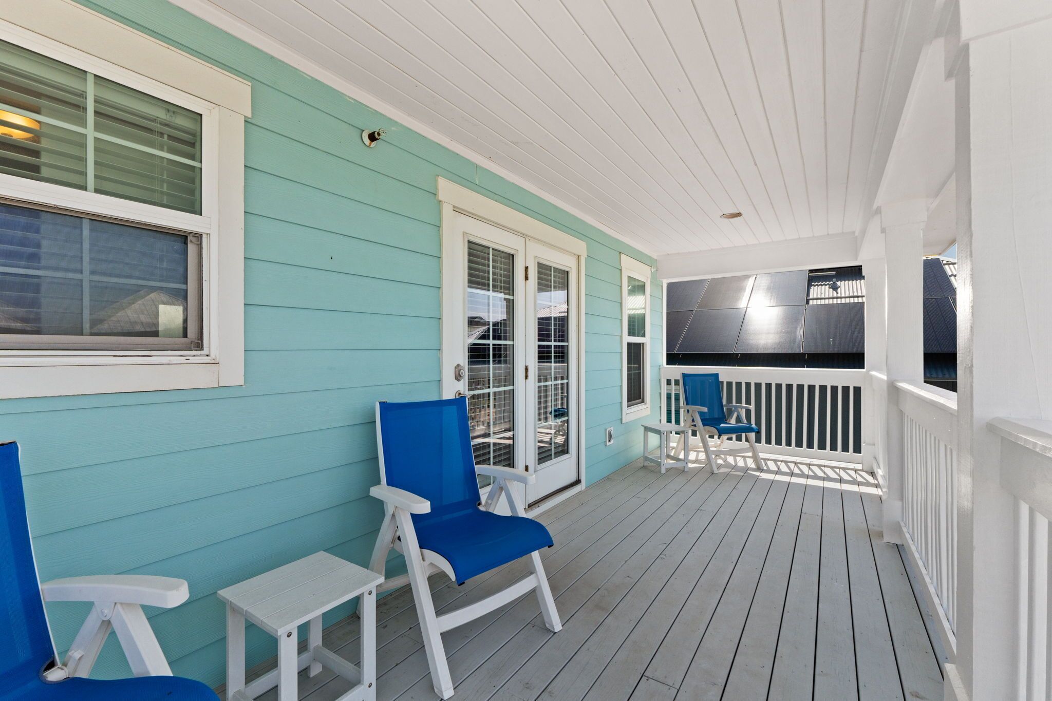 A covered porch with two chairs and a small table, a door with glass panels, and a railing.