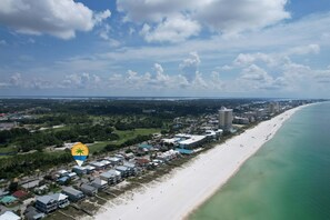 An aerial view of a coastal area with a beach, buildings, and greenery.