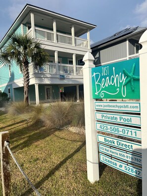 A two-story house with a balcony, a private pool, and a sign advertising 'Just Beachy' with contact information.